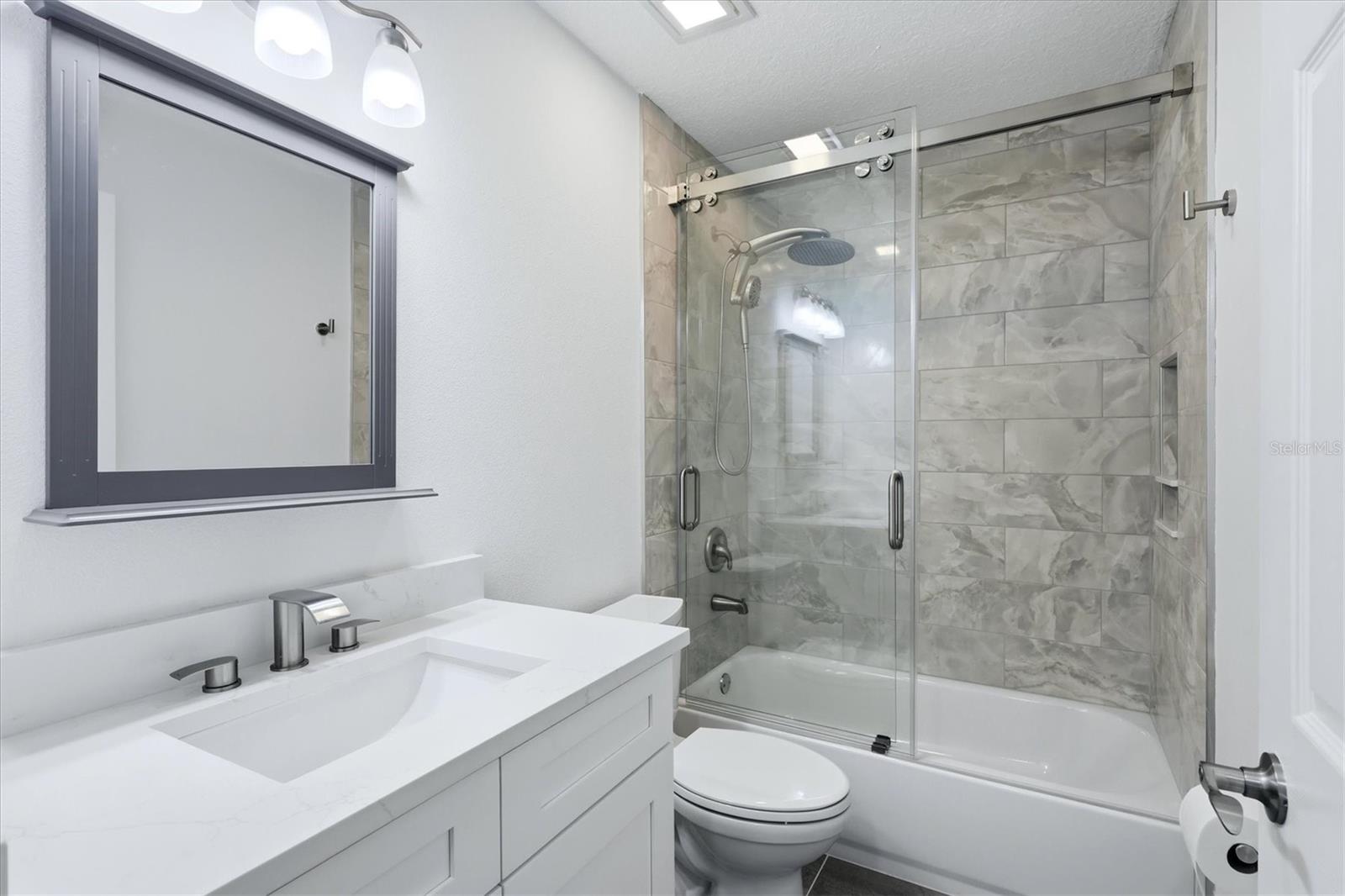 Secondary bathroom with newly tiled shower and glass sliding door as well as a quartz vanity with soft close cabinets and a picture mirror