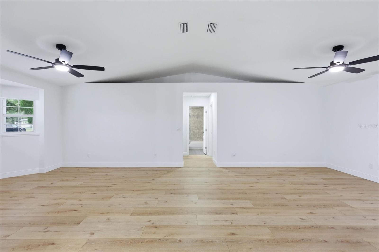 Living room/great room space features plant shelf with electric outlet.  Hallway leads to secondary beds and bath