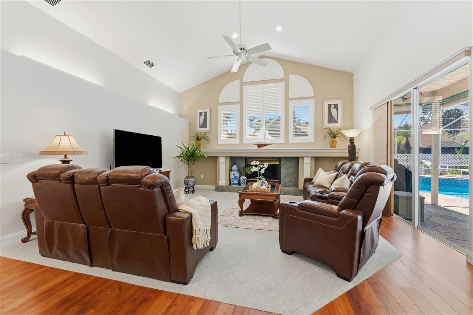 Great room with electric fireplace, cathedral ceiling, statement windows and pool views!