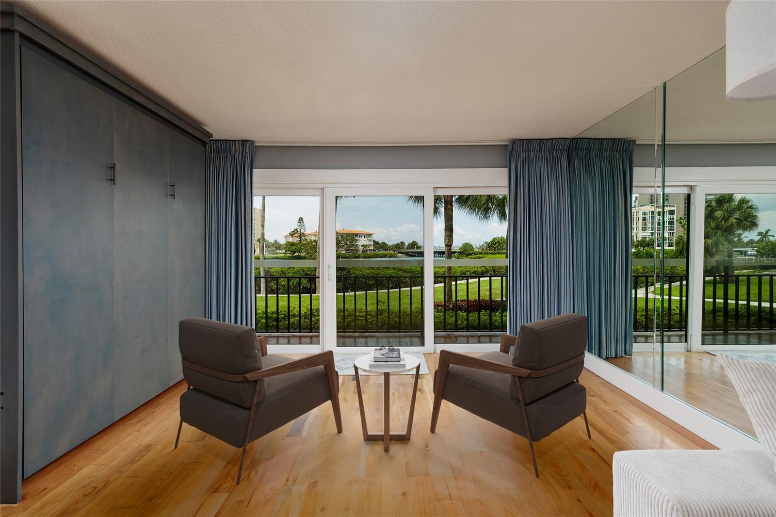 Virtual staged. Extended living room aeea with Murphy bed, hurricane impact slider, view of landscaping and water