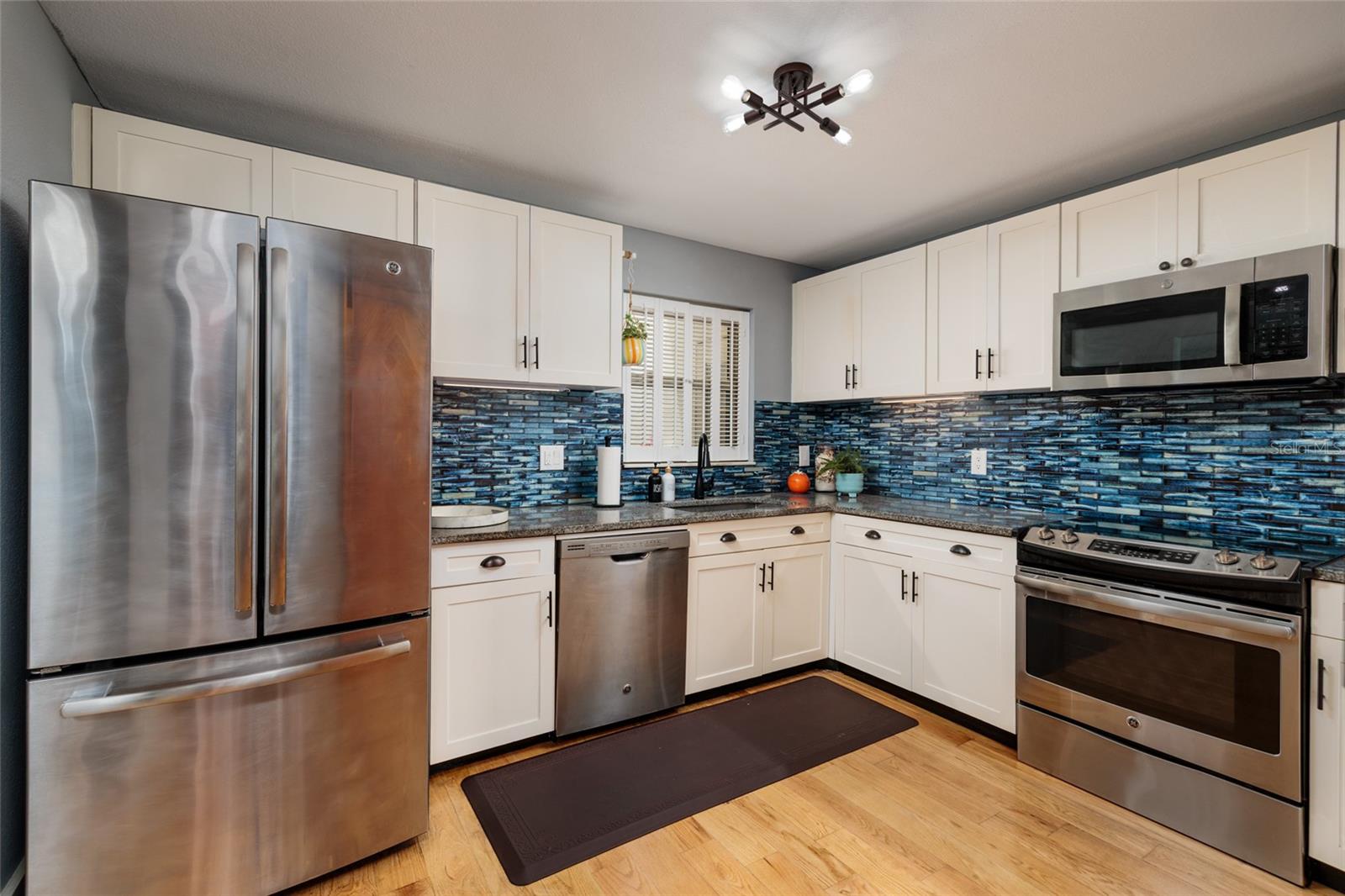 Kitchen with hurricane window, updated cabinets, stone countertop, tiled backsplash and stainless steel appliances.
