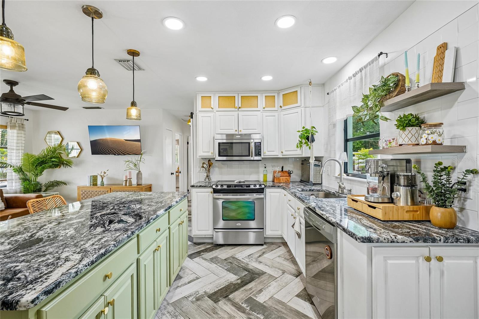 Kitchen — Kitchen with white cabinetry, dark granite countertops, subway tile backsplash, stainless steel range, built-in microwave, and open floating shelves. Green beadboard island with matching granite countertop and amber glass pendant lights above.