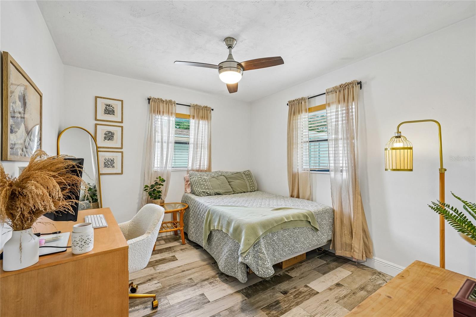 Bedroom 1 — Bedroom with tile flooring, ceiling fan, and two windows with blinds and sheer curtains. Room accommodates a queen bed and desk area.