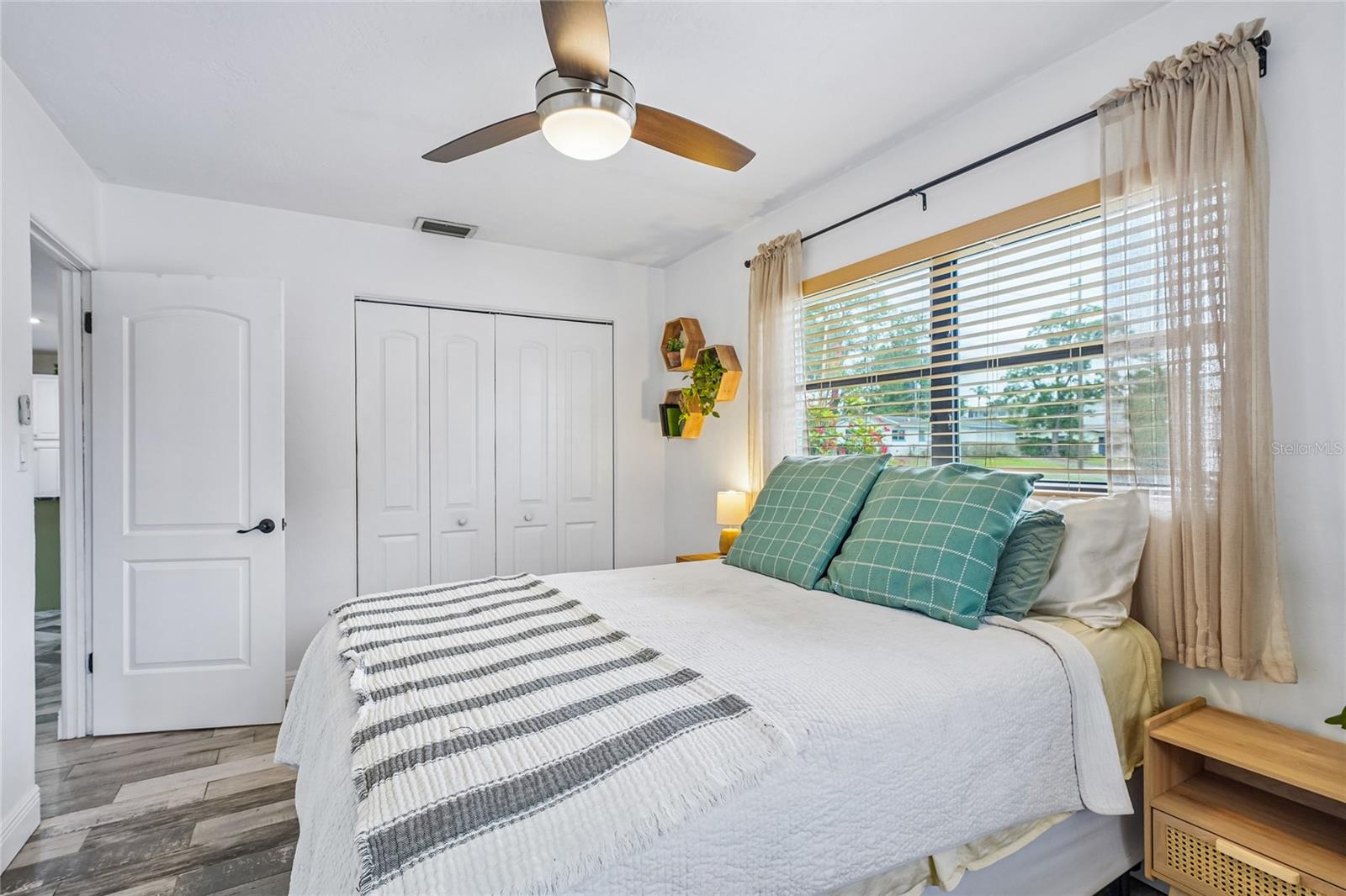 Bedroom 2 — Second view showing the reach-in closet with bi-fold doors, tile flooring, and ceiling fan. Window with blinds and sheer curtains.