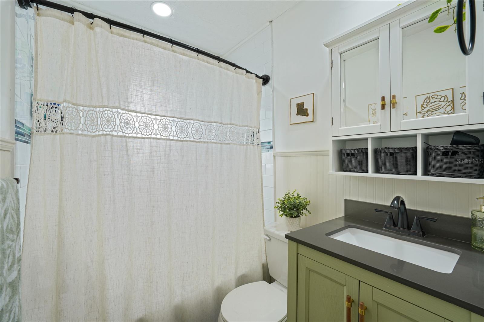 Bathroom — Second view showing the green vanity, dark countertop, undermount sink, matte black faucet, and beadboard wainscoting. Tile flooring and white upper cabinetry with brass hardware visible.