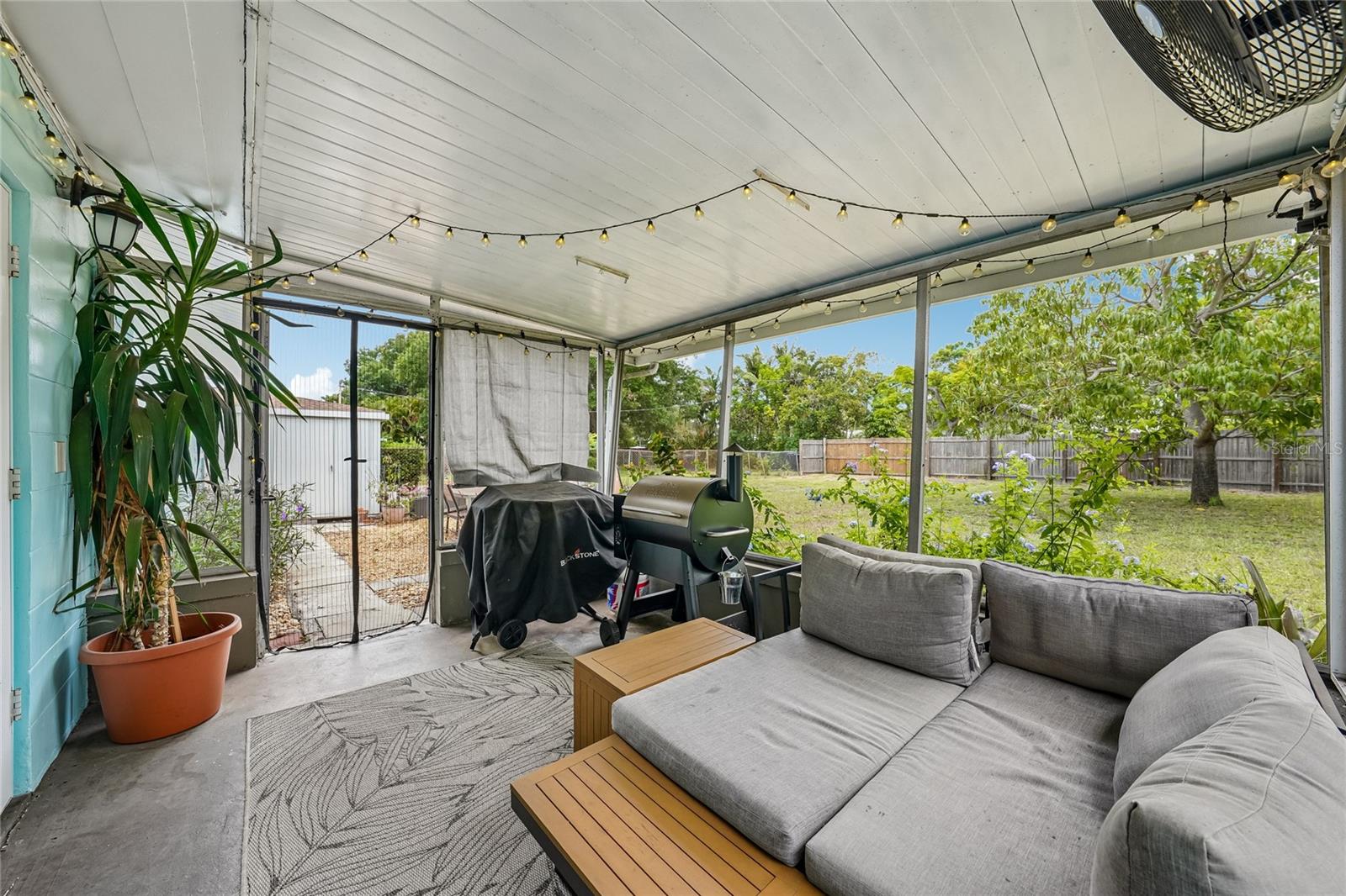 Screened lanai with concrete flooring and string lights. Fenced backyard with mature trees