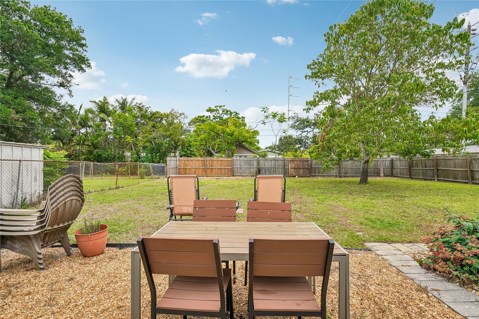 Backyard — Fenced backyard with gravel patio area, mature trees, and open lawn. Paver walkway along the perimeter.
