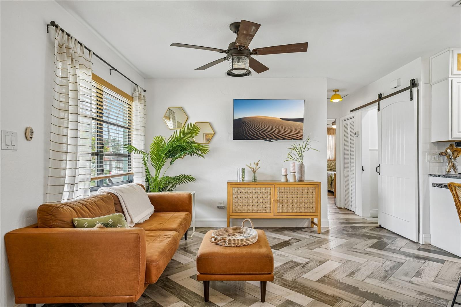 Living Room — Wide-angle view of the living area showing the full herringbone tile floor pattern, ceiling fan, and large windows with natural light.