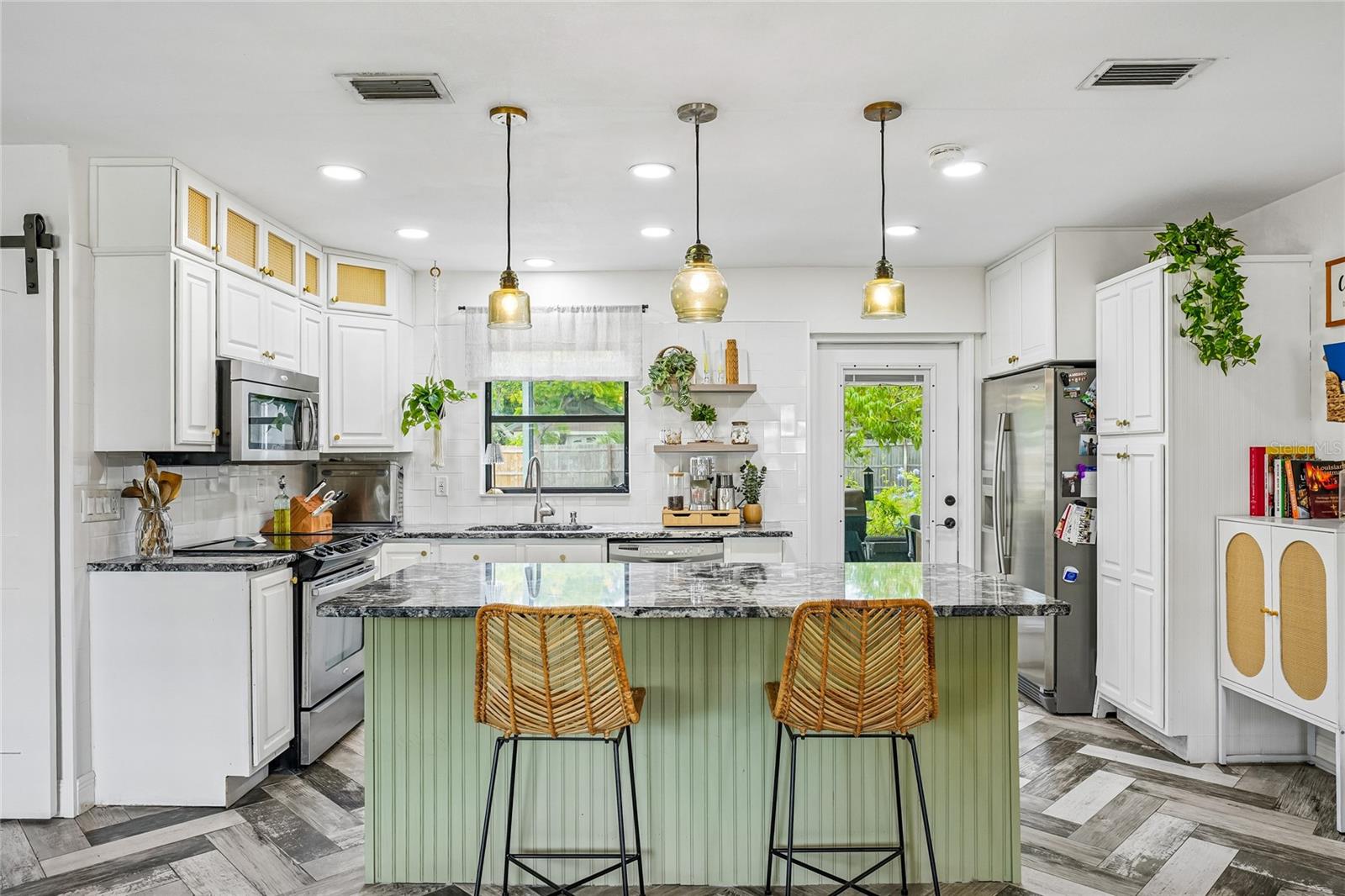 Kitchen. White shaker-style cabinetry, dark granite countertops, subway tile backsplash, and stainless steel appliances including range and French door refrigerator. Green beadboard center island with seating and three amber glass pendant lights.