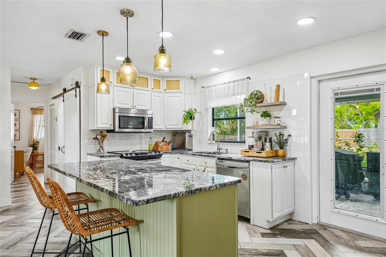 Kitchen. Dark granite island countertop, stainless steel range, stainless steel dishwasher, and open floating shelves with subway tile surround. Exterior door to screened patio