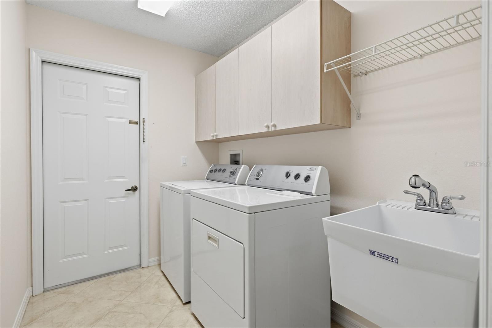 Indoor laundry room with utility sink, storage cabinets and easy-clean tile. Exit  door to garage.