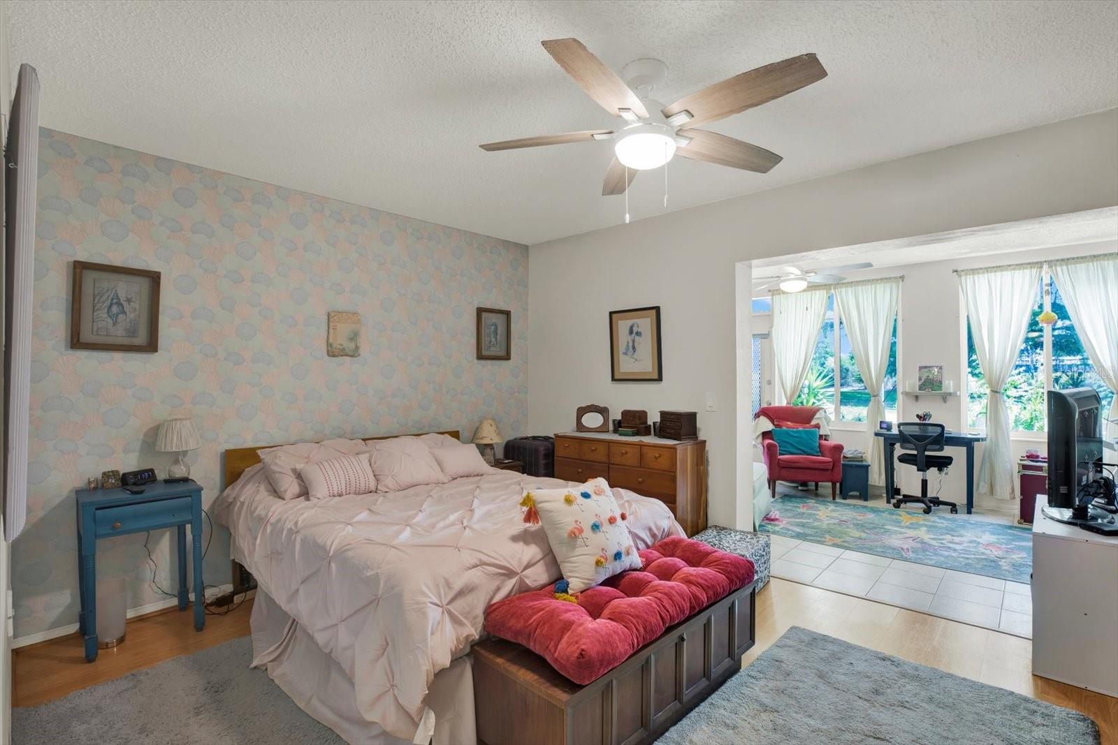 Primary bedroom with ceiling fan open to Florida room with garden views.