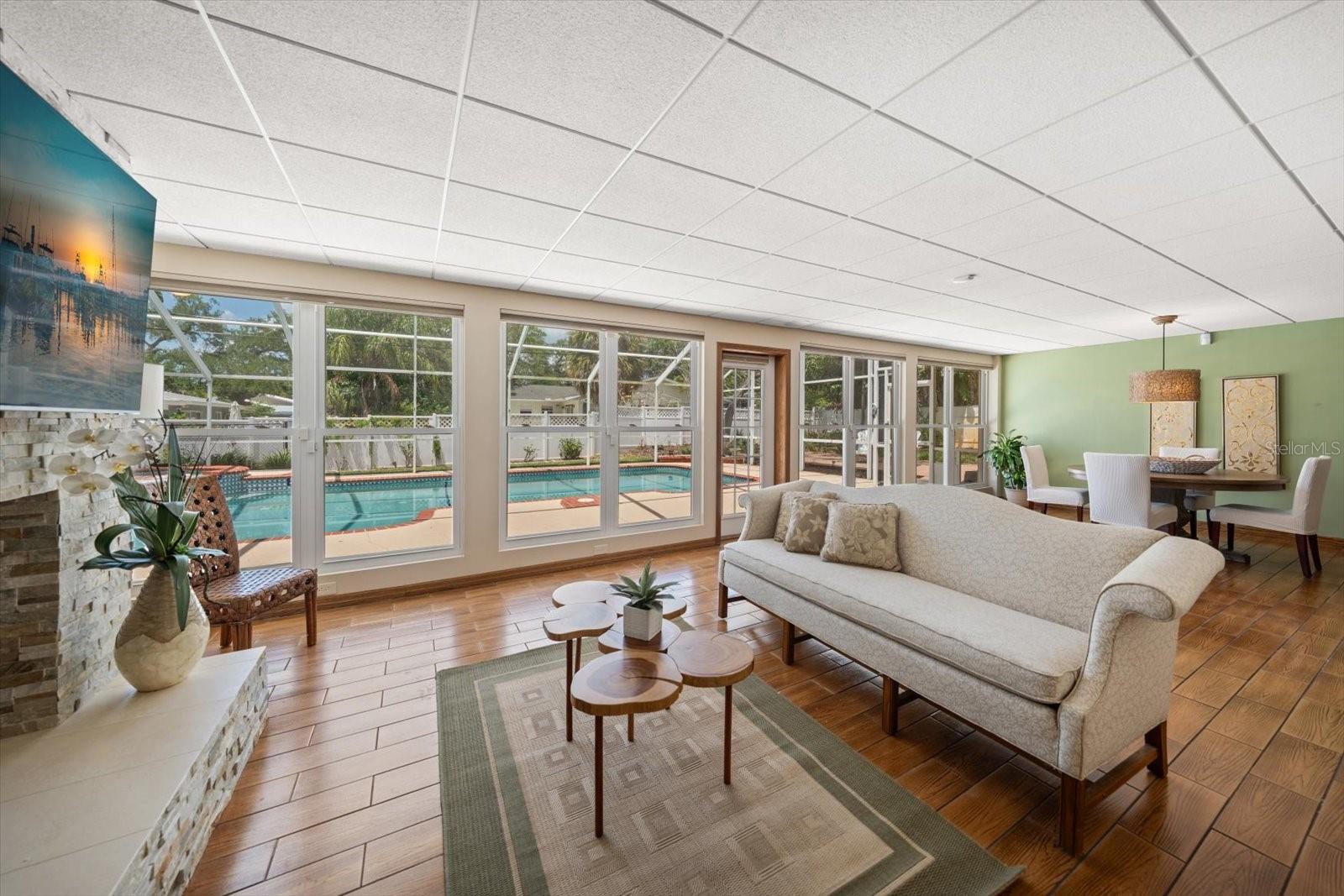 A bright and versatile great room offers stunning views of the sparkling pool area through an expansive wall of windows and sliding glass doors, filling the space with natural light and creating a seamless indoor-outdoor connection.