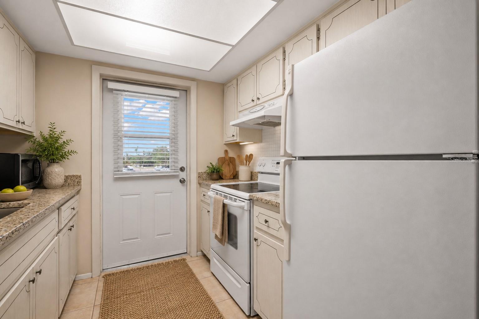 Virtual staging. Kitchen with granite counters, mosaic tile backsplash, large single basin sink with pull out sprayer, fridge, range, microwave