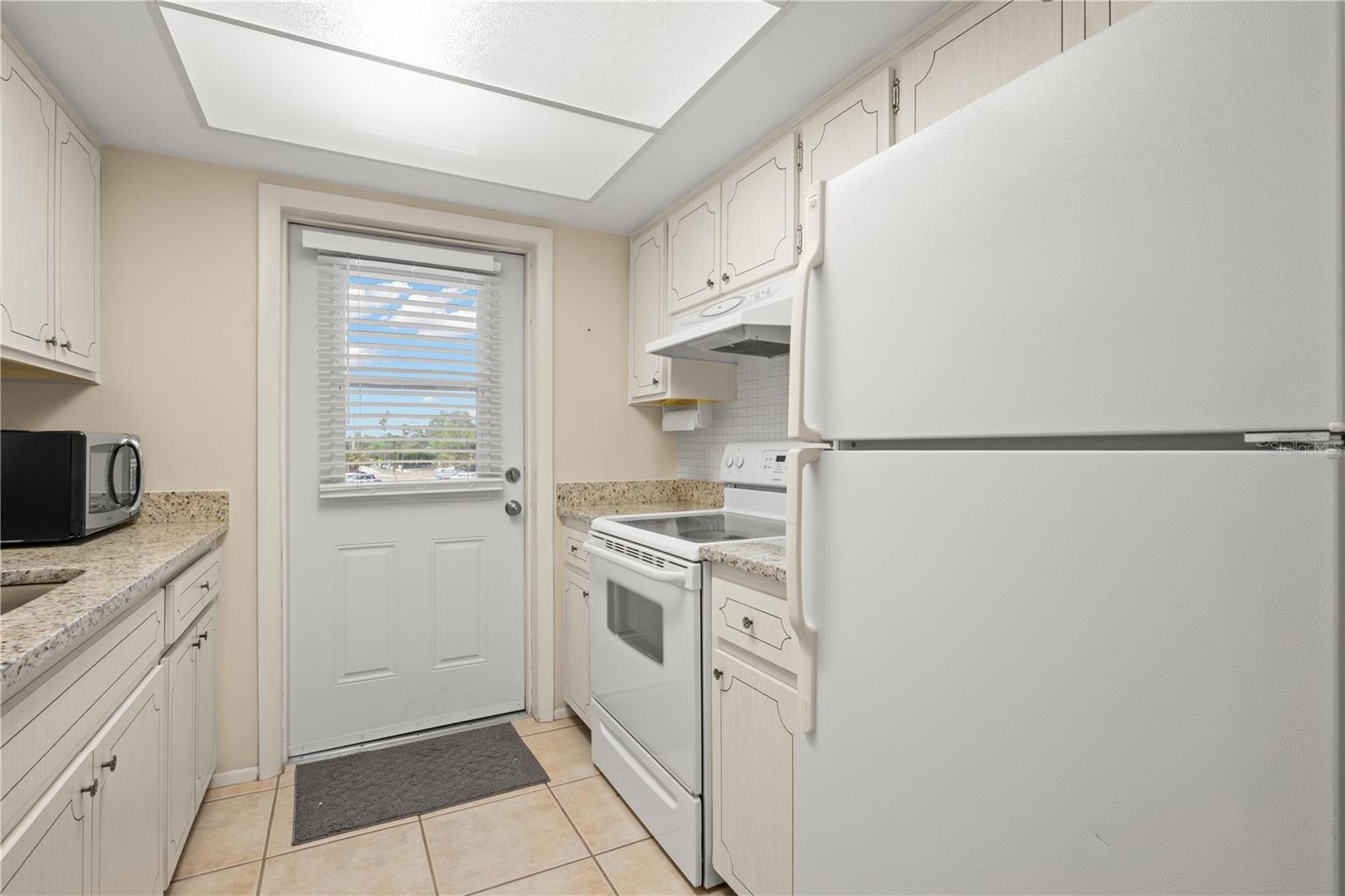 Kitchen with granite counters, mosaic tile backsplash, large single basin sink with pull out sprayer, fridge, range, microwave