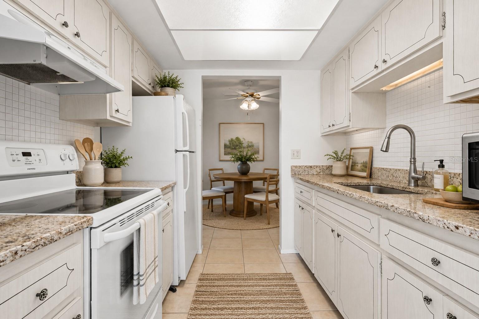 Virtual staging. Kitchen with granite counters, mosaic tile backsplash, large single basin sink with pull out sprayer, fridge, range, microwave
