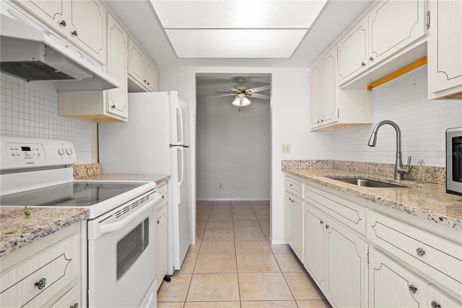 Kitchen with granite counters, mosaic tile backsplash, large single basin sink with pull out sprayer, fridge, range, microwave