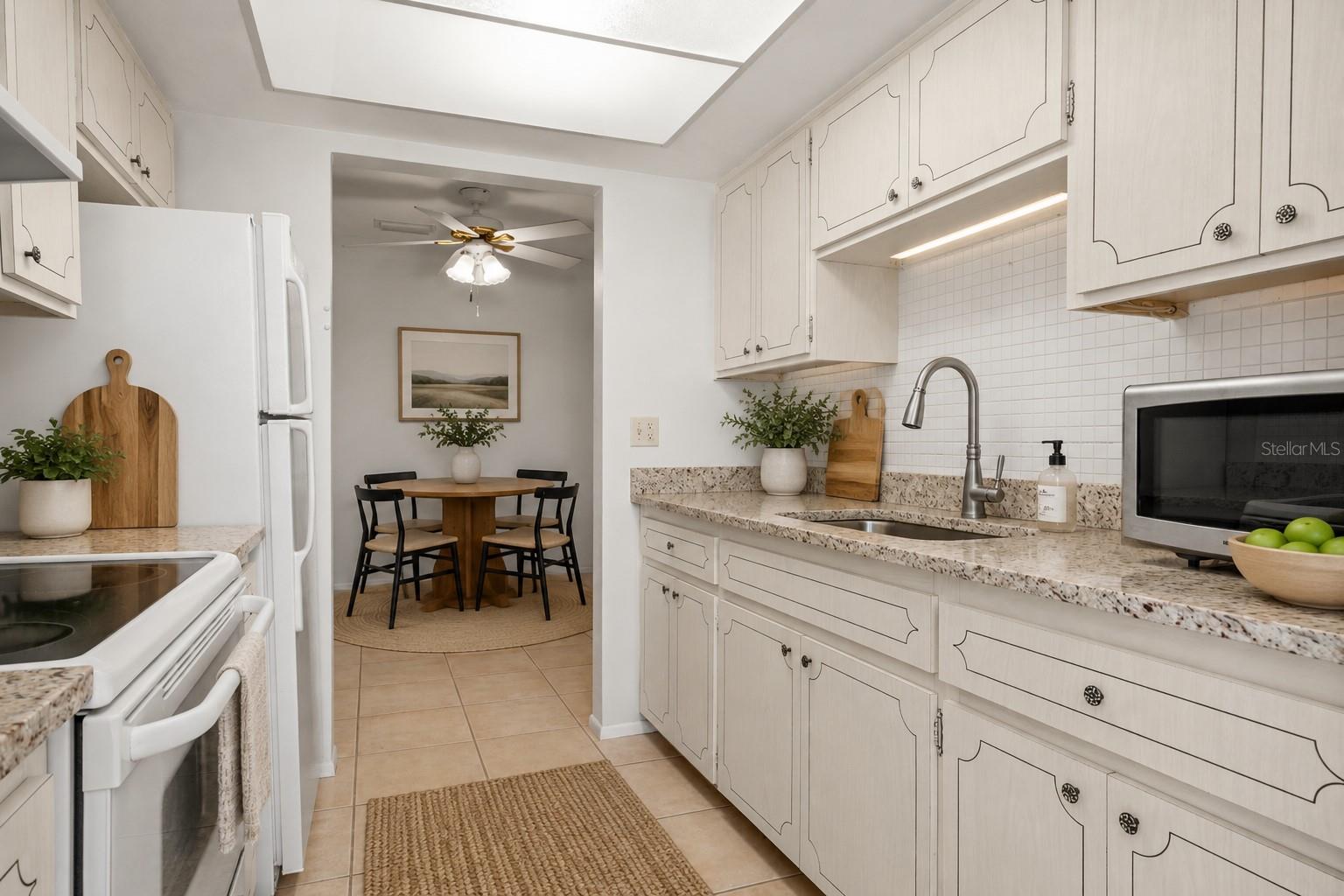 Virtual staging. Kitchen with granite counters, mosaic tile backsplash, large single basin sink with pull out sprayer, fridge, range, microwave