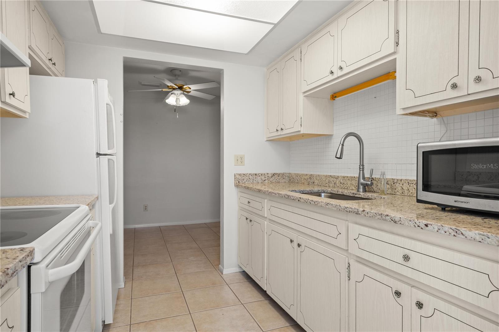 Kitchen with granite counters, mosaic tile backsplash, large single basin sink with pull out sprayer, fridge, range, microwave