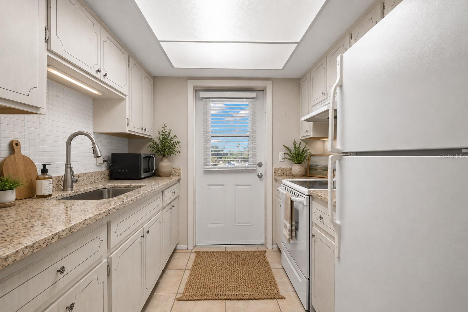 Virtual staging. Kitchen with granite counters, mosaic tile backsplash, large single basin sink with pull out sprayer, fridge, range, microwave