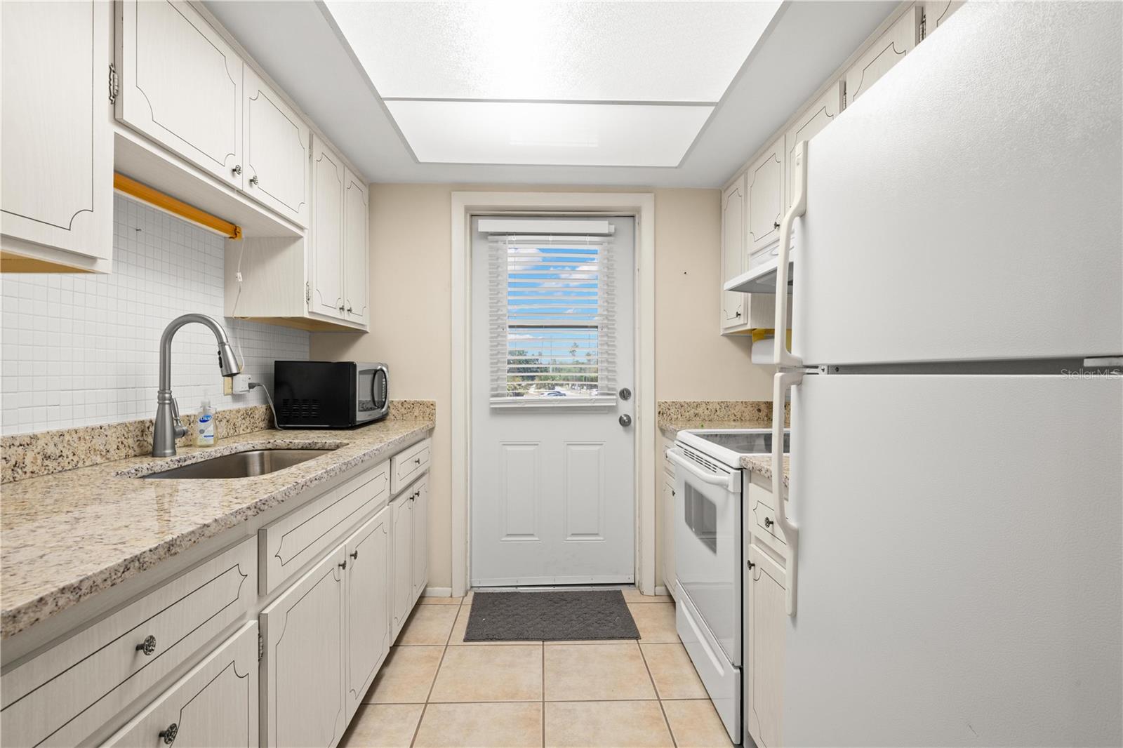 Kitchen with granite counters, mosaic tile backsplash, large single basin sink with pull out sprayer, fridge, range, microwave