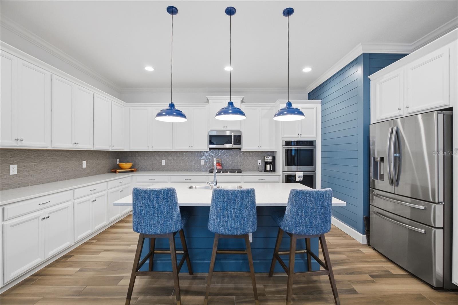 Tons of storage, breakfast bar, quartz counters, double ovens, custom tile backsplash, custom blue shiplap & pendant lighting all add to this gourmet kitchen.