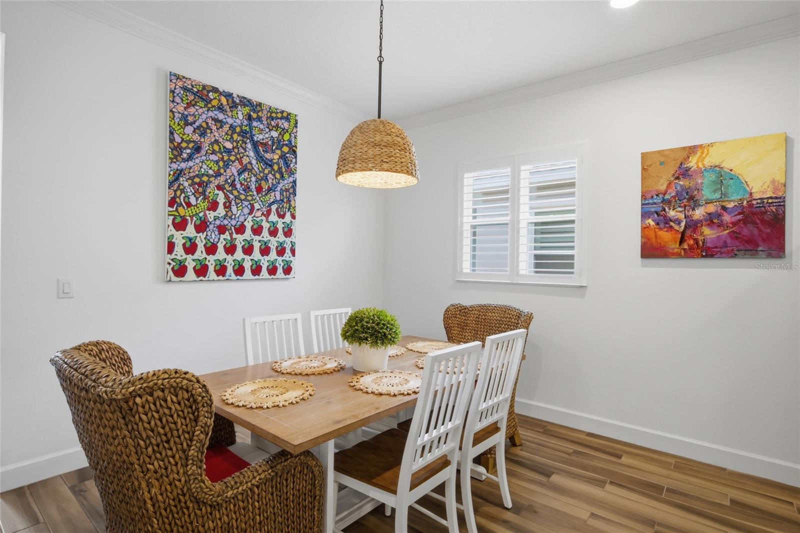Dining room adorned with custom pendant style light fixture and double window with plantation shutters allowing natural light to fill the space.