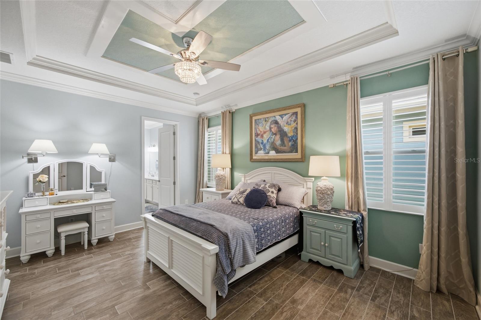 Primary Bedroom Suite with crown molding, tray ceilings, custom fan and large windows with plantation shutters.