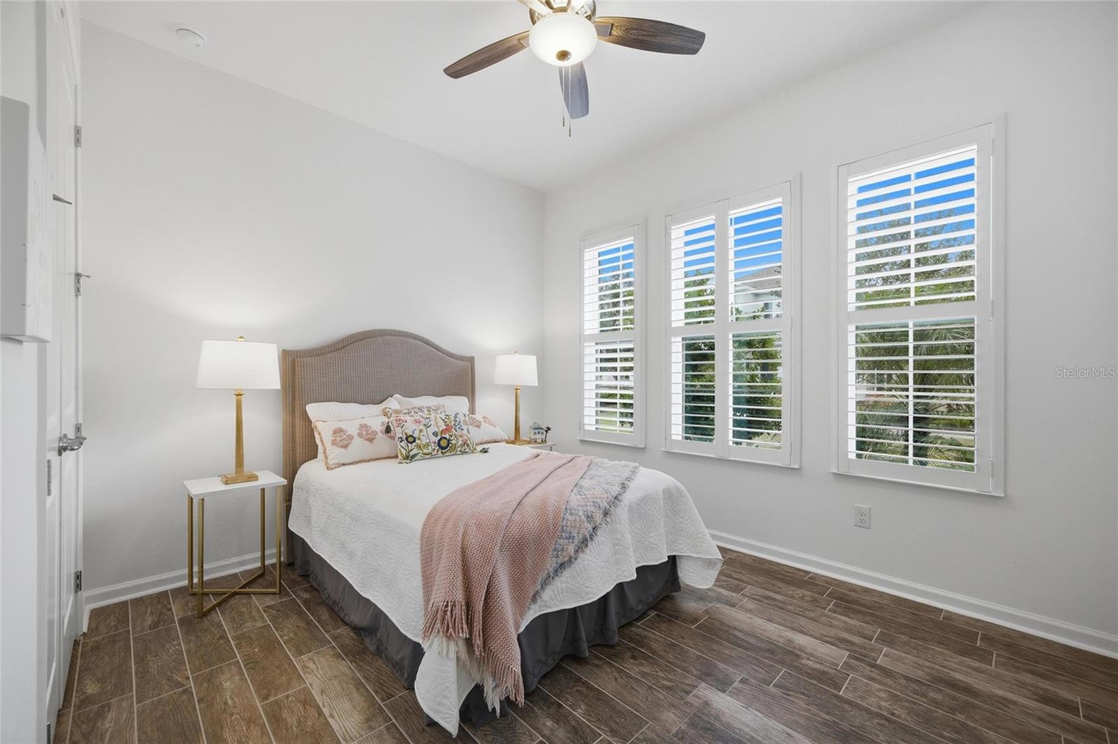 Bedroom 3 with gorgeous natural light, plantation shutters & ceiling fan at front of home, looking out to the green space.