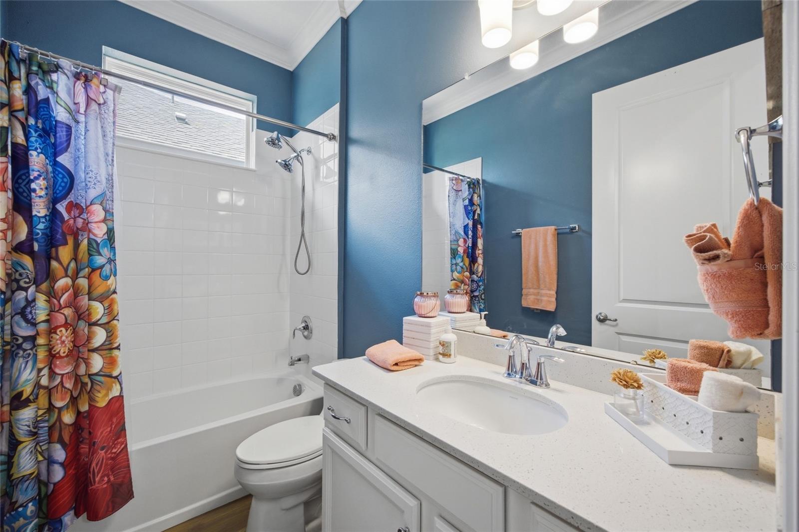 Second bathroom with quartz counters tiled tub / shower combo with a window allowing natural light to come in.