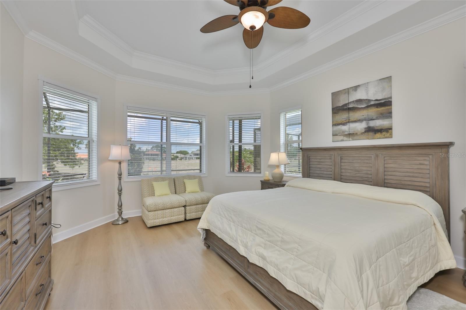 Primary Bedroom is oversized, with trey ceilings, modern flooring and large windows for natural sunshine and overlooking the patio and pool.