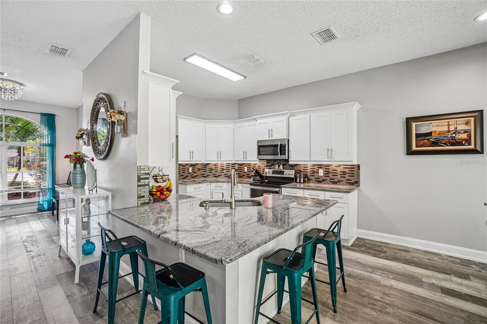 Kitchen — White shaker cabinetry with granite countertops, a mosaic tile backsplash, and a large peninsula with breakfast bar seating for four. Stainless steel appliances and open great room.