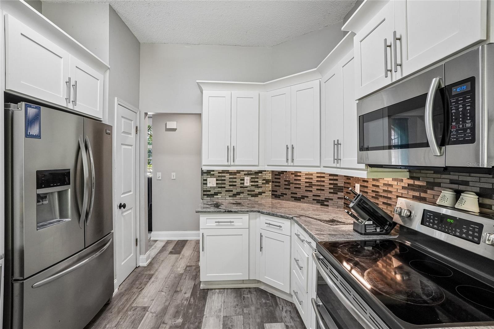 Kitchen — Kitchen work zone with white shaker cabinetry, granite countertops, mosaic tile backsplash, and stainless steel double-oven range and over-the-range microwave. French door refrigerator with ice and water dispenser