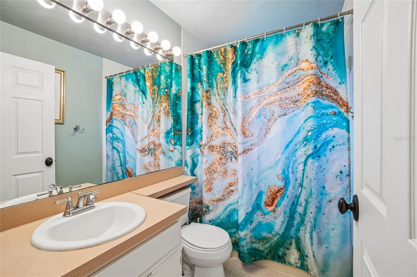 Bathroom 2 — Full bathroom with single-sink vanity, solid surface countertop, Hollywood-style vanity light strip, full-width mirror, and a tub/shower combination.