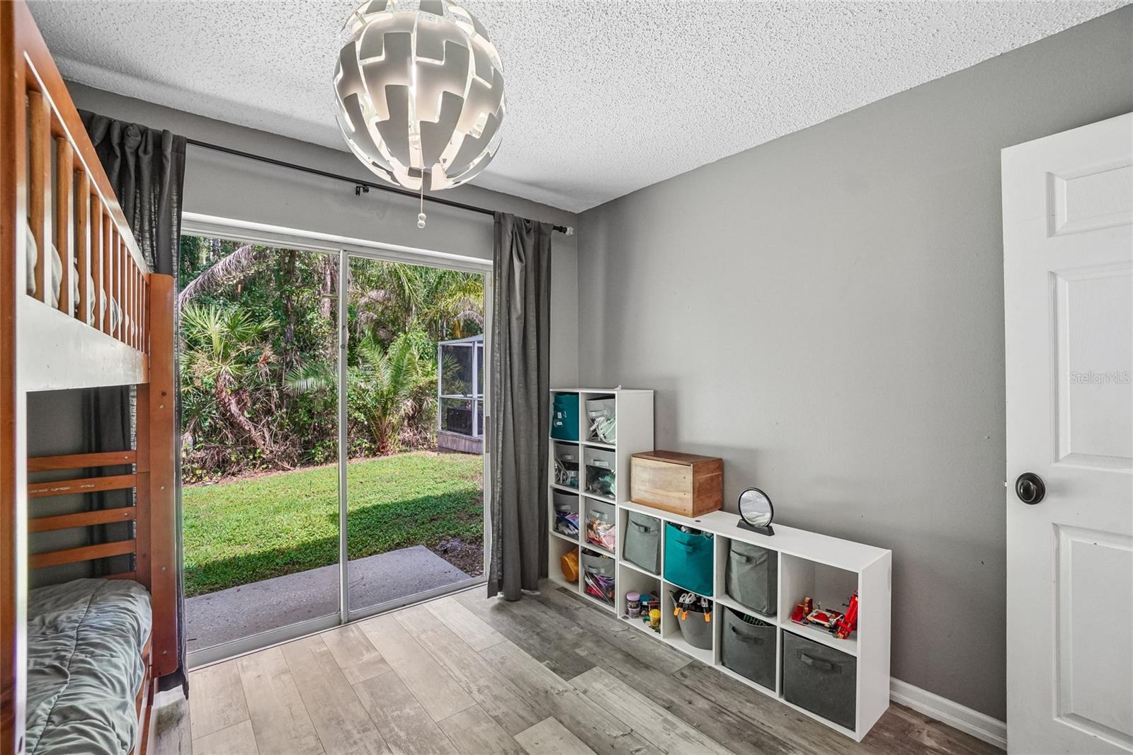 3rd bedroom with luxury vinyl plank flooring, a pendant light fixture, and a sliding glass door with direct access to the backyard. Conservation views of mature palms and tree canopy are visible through the glass.