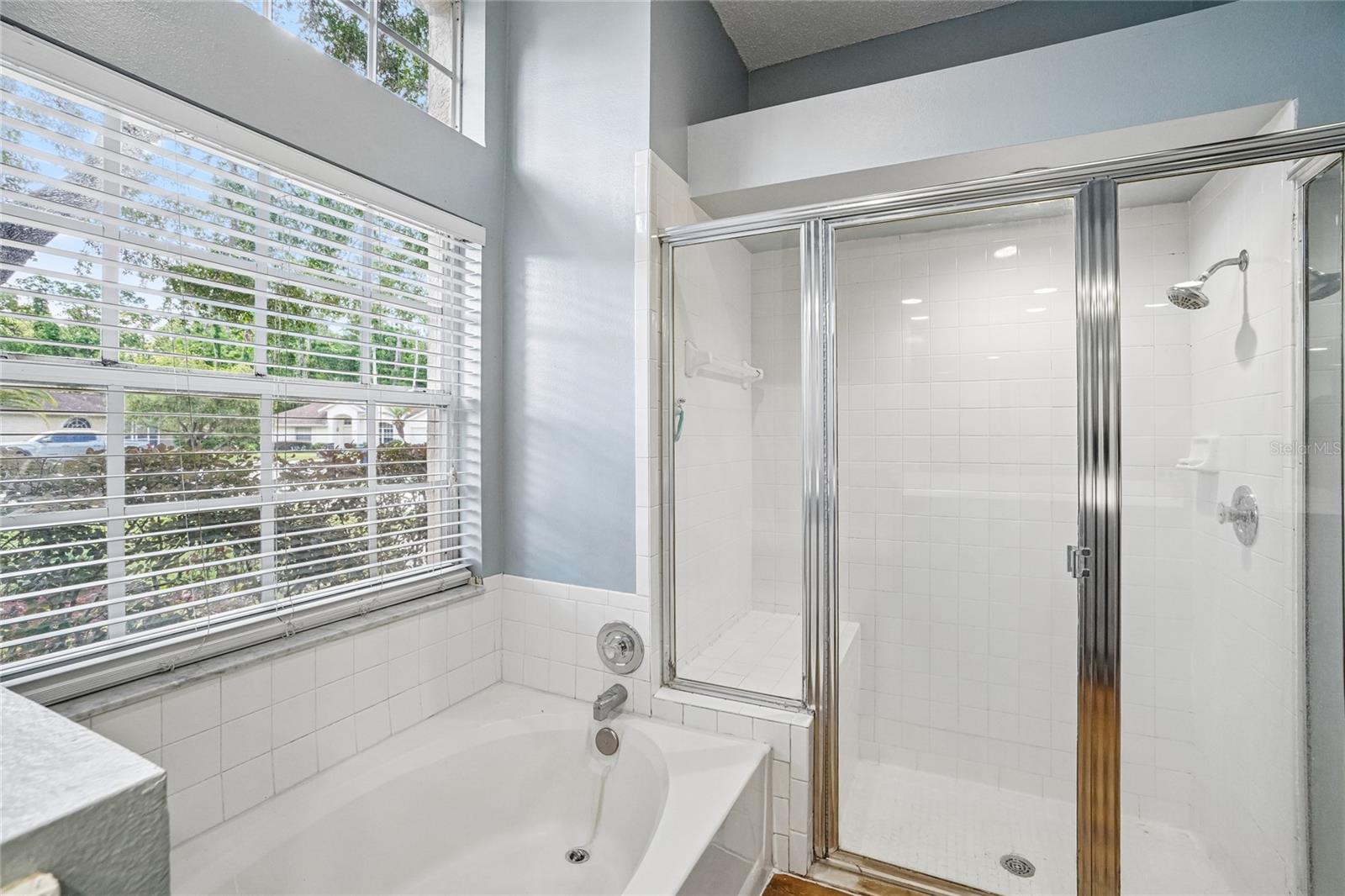 Primary bathroom — with a soaking tub featuring tile surround, a separate glass-enclosed walk-in shower with white tile walls