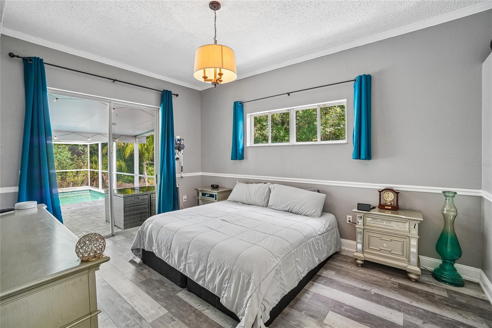Primary bedroom with luxury vinyl plank flooring, crown molding, a pendant light fixture, and a window with natural light. Sliding glass door leads to the primary bathroom hallway and closet doors.