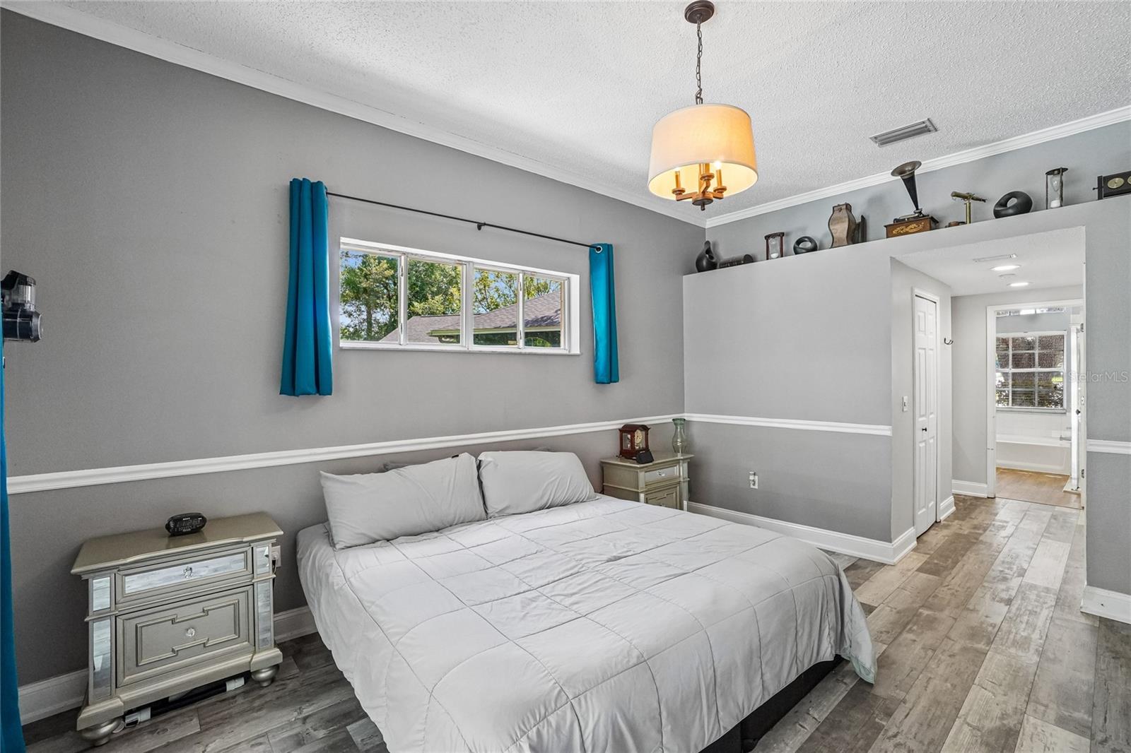 Primary bedroom with luxury vinyl plank flooring, crown molding, a pendant light fixture, and a sliding glass door with direct access to the screened pool enclosure
