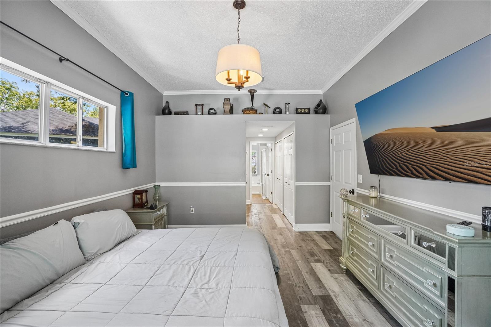 Primary bedroom — Primary bedroom with luxury vinyl plank flooring, crown molding, a pendant light fixture, and a window.