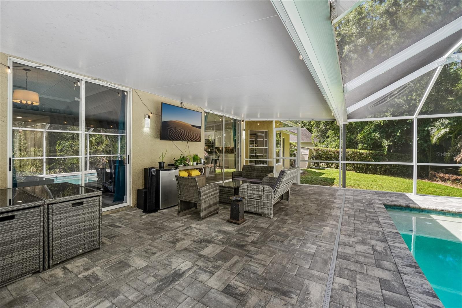 Screened lanai — Covered screened lanai with pavered deck and outdoor seating area adjacent to the pool. Sliding glass doors connect to the interior, with the fenced backyard and conservation tree line visible beyond the enclosure.