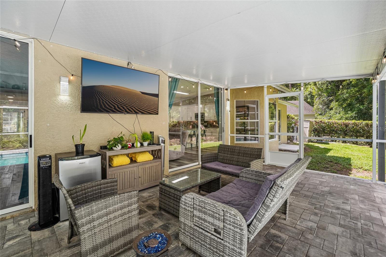 Screened lanai — Covered screened lanai with pavered deck and a separate seating area adjacent to the pool. Sliding glass doors open to the kitchen and great room, with backyard grass and mature tree canopy visible through the screen.