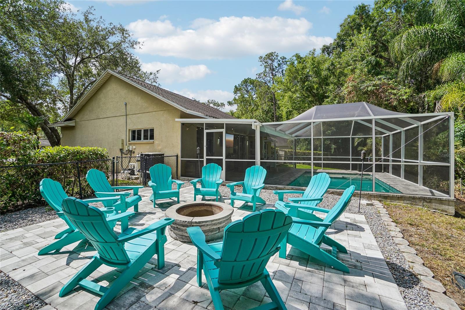 Backyard / fire pit area — Pavered fire pit patio with seating area adjacent to the screened pool enclosure. Mature oak canopy, a privacy hedge