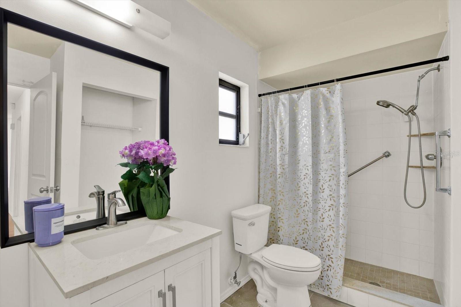 Tastefully updated guest bathroom featuring a crisp white vanity and a spacious, walk in shower.