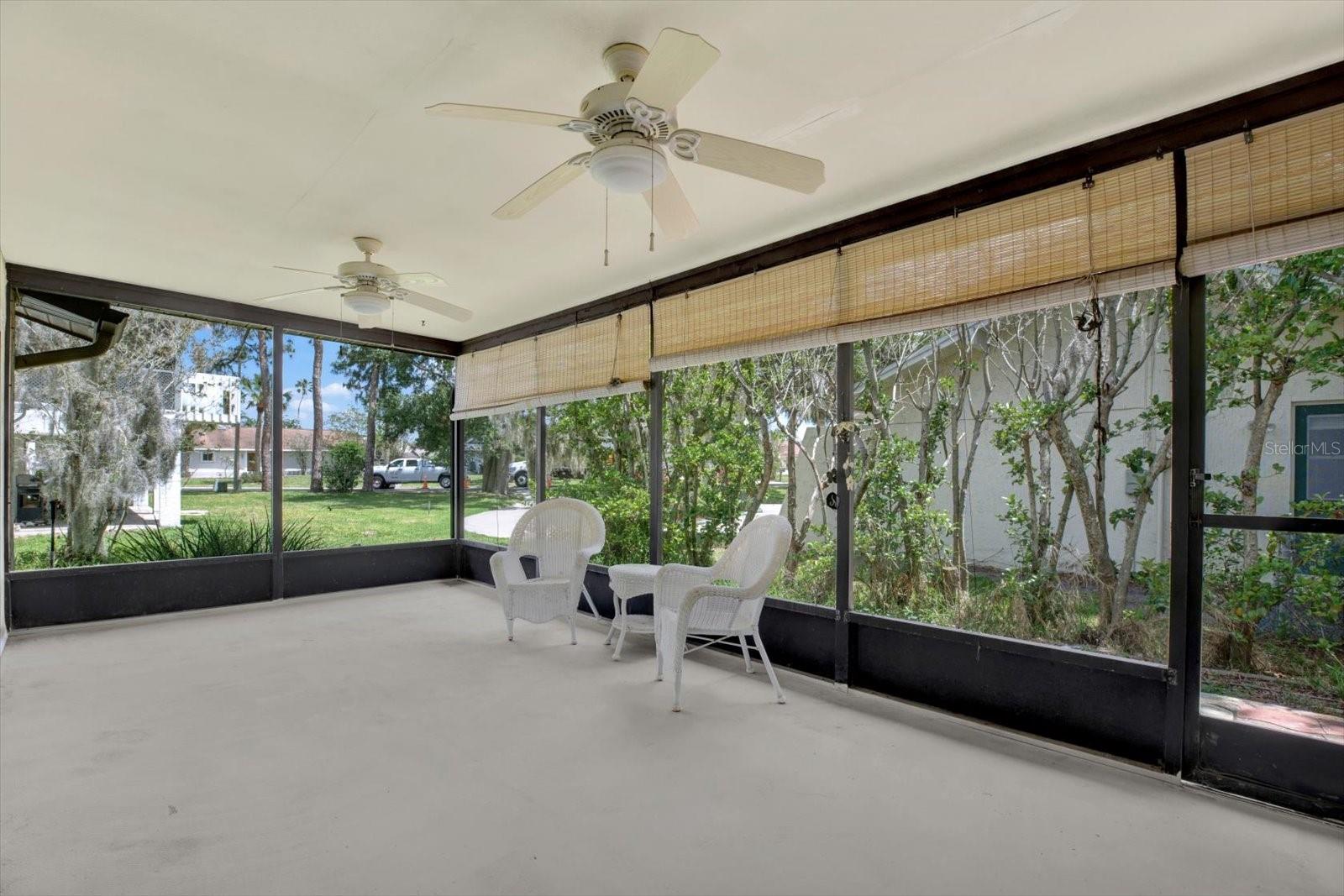 Expansive, screened in lanai featuring dual ceiling fans and roll down shades, providing the perfect shaded space for outdoor relaxation.