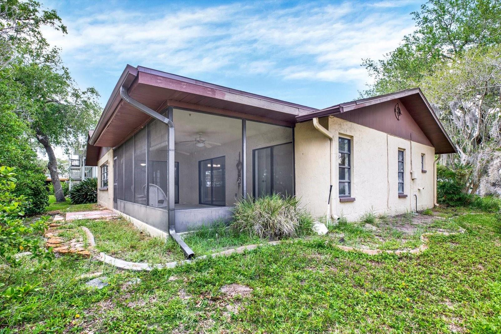 Rear exterior view highlights the massive screened in lanai and a spacious backyard bordered by big trees offering more shade and privacy.
