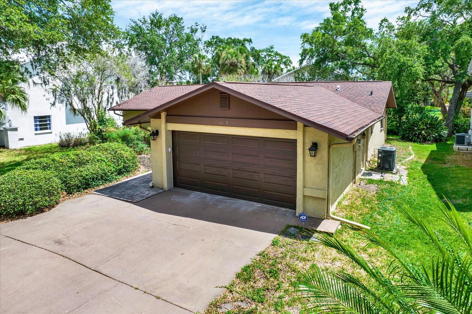 Front exterior showcasing a wide concrete driveway leading to a spacious attached two car garage surrounded by landscaping.