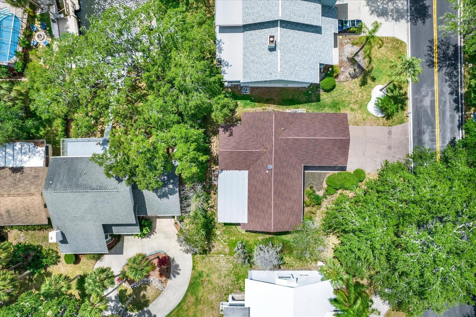 Birds Eye aerial view showcasing the homes roofline, private lot layout, and lush tree canopy surrounding the property.