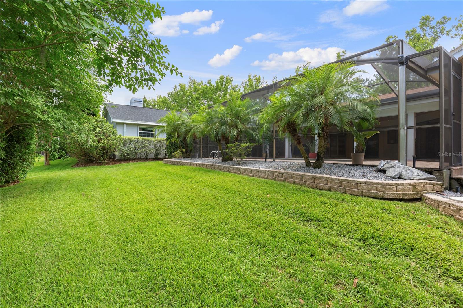 Private backyard oasis with lush tropical landscaping perfect for relaxing or entertaining year-round. A charming stepping-stone walkway is framed by low-maintenance landscaping, featuring large decorative rocks for a clean, natural, and easy-care backyard.