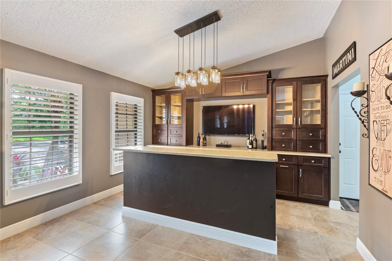 Dedicated room featuring formal built-in cabinetry and an elegant countertop bar with matching pendant lighting, offering the ideal space for entertaining guests or creating a relaxing lounge retreat.