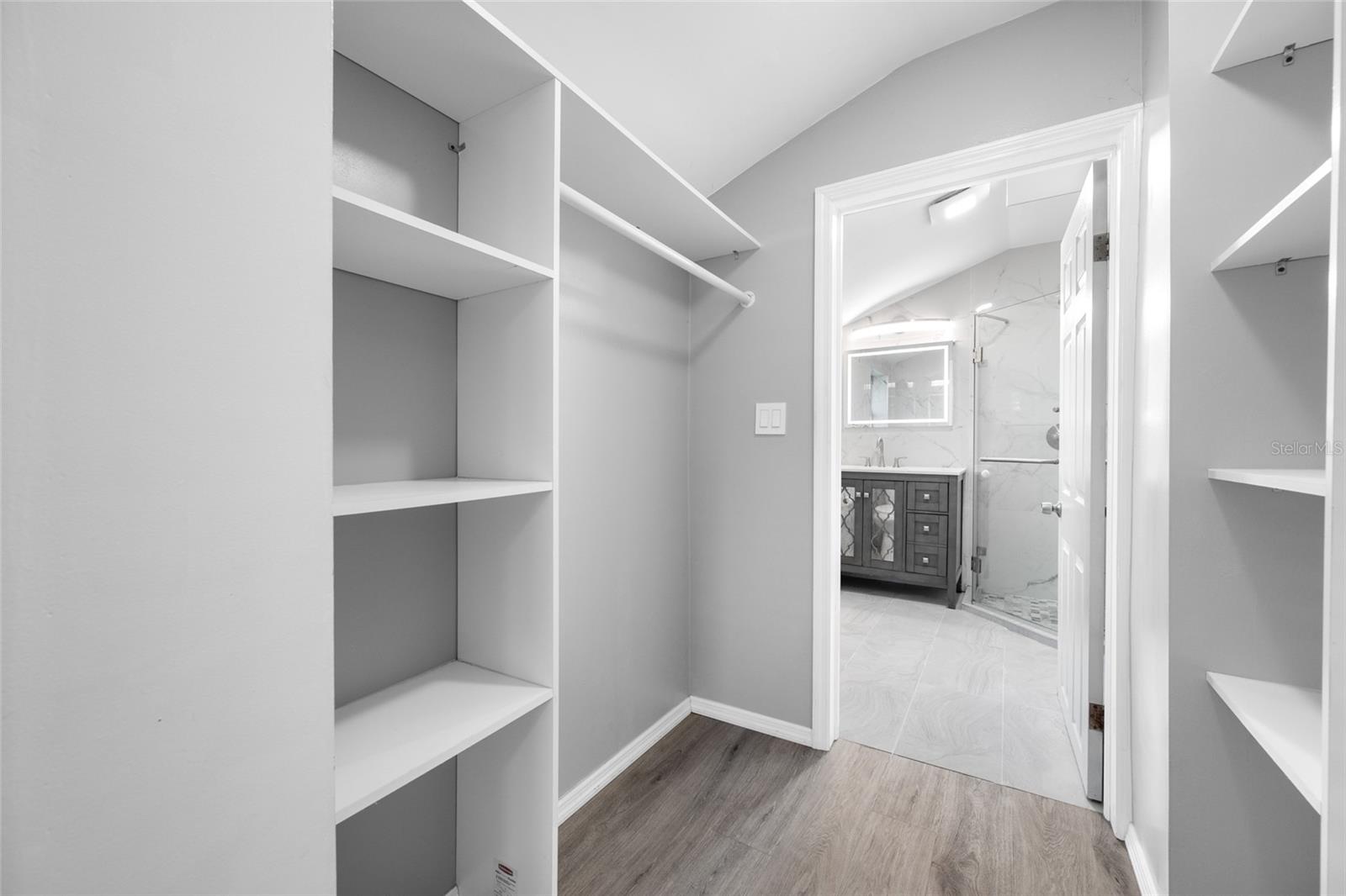 Primary Bedroom suite with walk-in closet, with built in shevles, that opens through to private en-suite updated bathroom with marble tile and glass shower.